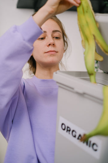 Person placing a banana peel into an indoor organic waste bin in a kitchen